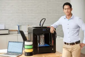 man standing next to a 3d printer filament and laptop